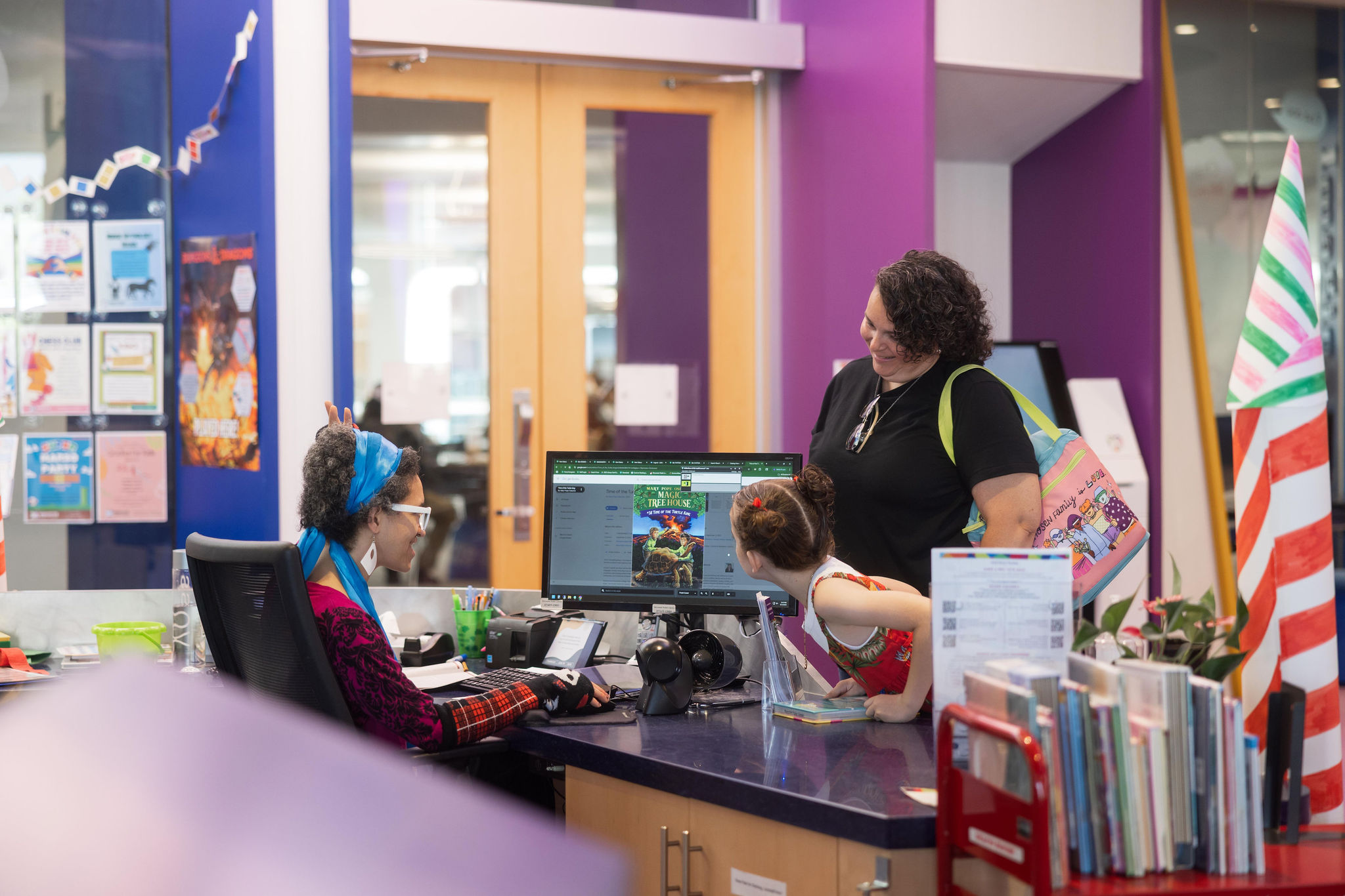 A librarian helps a child at the service desk.