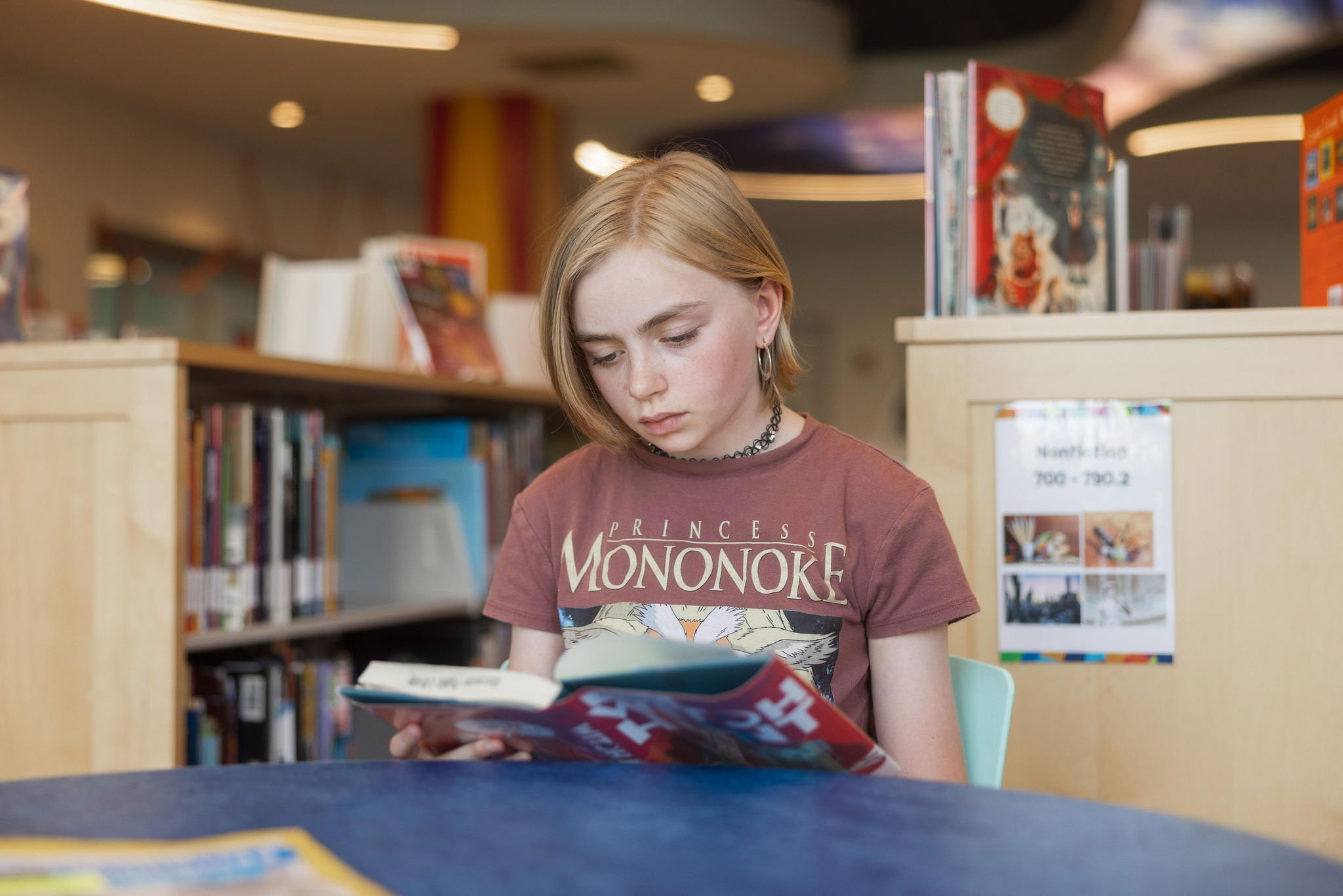 A young person sits at a table in the tween section and reads a book.