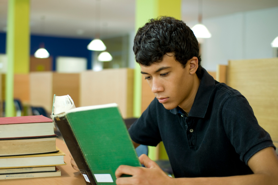 A teen reading a book in a library, points to recommendation for teens page.